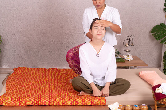 Young Asian woman receiving traditional Thai head and shoulder massage by professional therapist on mat in spa salon. Relaxing wellness, health care, and alternative medicine concept.