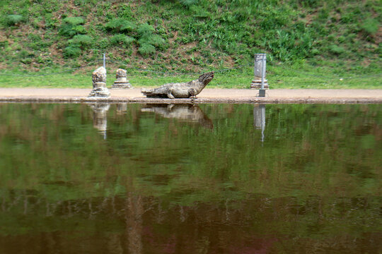 Statua in pietra di un coccodrillo a bordo vasca riflessa sulla superficie dell'acqua nell'area archeologica del Canopo a Villa Adriana, Tivoli, Italia