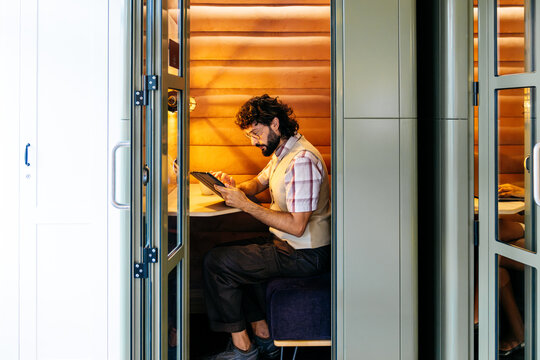Male professional working with a digital tablet inside a soundproof office pod in a contemporary coworking space