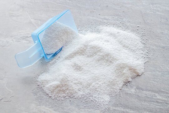 Household chemicals. Washing powder in plastic spoon on grey background