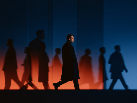 Man in a coat walking past shadows of other commuters