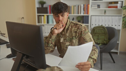 Obraz premium Man soldier holding paper and pen, squinting while reading at computer in office building; frustration paperwork.