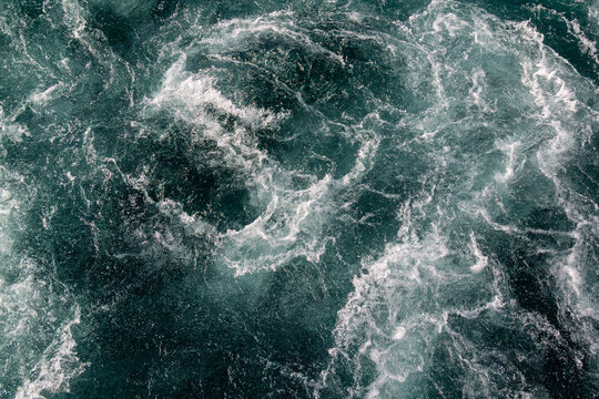 Dark turquoise swirling frothy water close-up. Pristine clear Waikato River, New Zealand flowing from Lake Taupō Control Gates, supporting downstream hydroelectric generation.