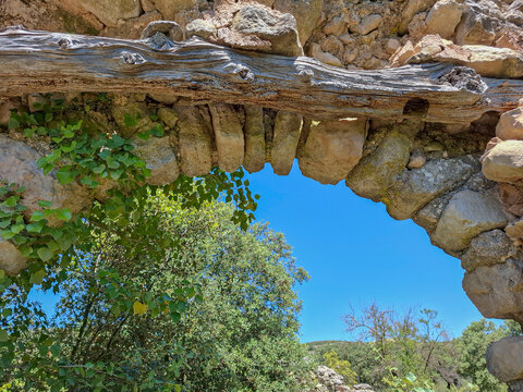Ruined stone arch with timber lintel and green plants under blue sky in an old site from the medieval period