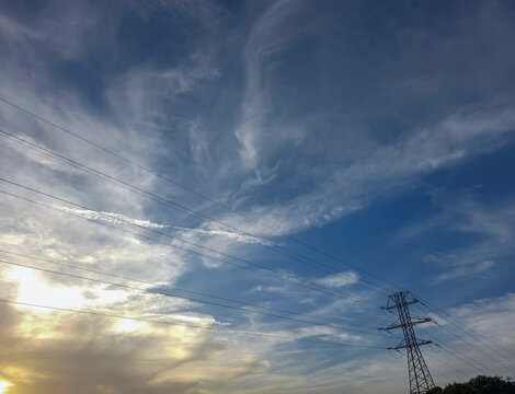 Silhouette of high voltage power line tower against evening sky with clouds at sunset in the background