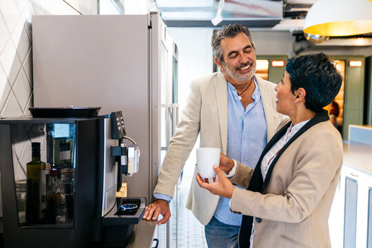 Two diverse business people enjoying a conversation and smiling while getting coffee from an automatic machine in a modern office