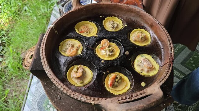 Hand adding shrimp into Vietnamese mini savory pancakes cooking in a traditional clay pan.