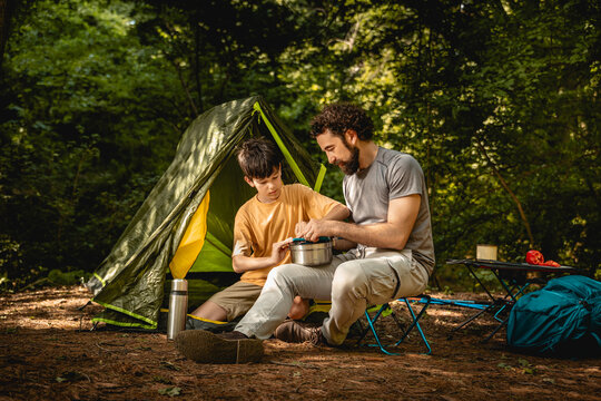 Father and son cook together at campsite in forest during daytime