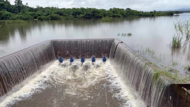 A concrete weir structure controls water flow in a rural river. The storage system features blue valves releasing stream current during irrigation supply management for agriculture.
