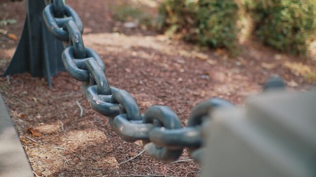 Close up metal chain with shallow depth of field shows interconnected links, metal texture and artistic background blur in a park environment