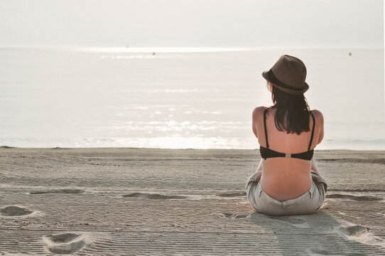 Rear view of a woman sitting on beach looking out to sea, Majorca, Balearics, Spain