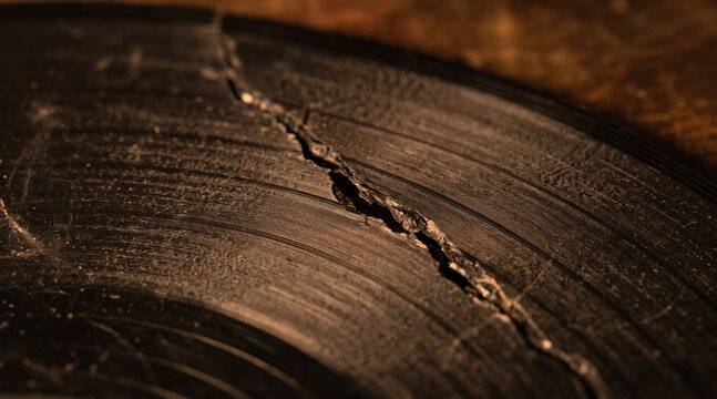 Close up of broken vinyl record with warm light highlighting the damage.