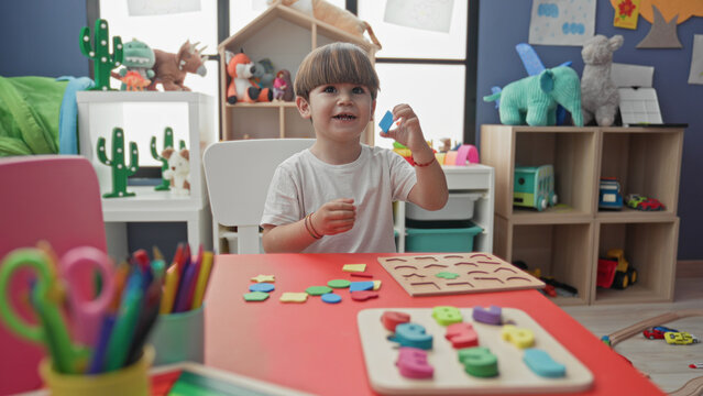 Boy places wooden puzzle piece with hand on table in building playroom; concentration learning play.
