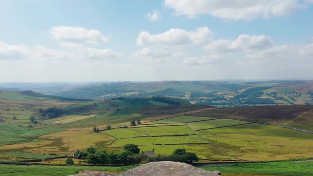 Panoramic mountain landscape with rolling green valleys beneath dramatic summer clouds. Scenic countryside vista from rocky summit across patchwork farmland and distant hills. Nature destination