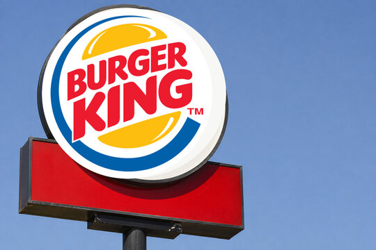 Illustrative editorial concept of a close-up Burger King roadside sign against a clear blue sky with copy space, representing quick-service restaurant branding.