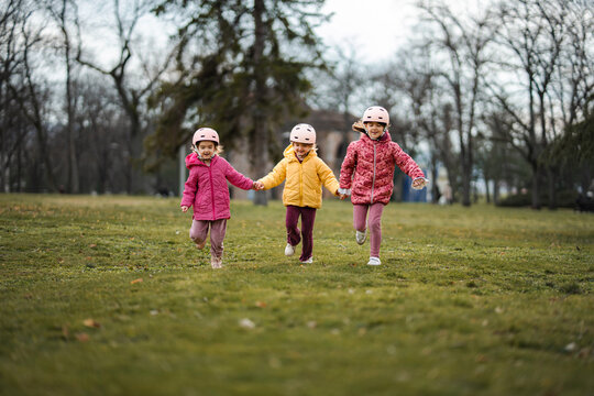 Three preschool age girls holding hands and running with joy in a park