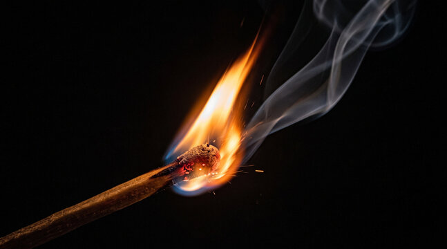 Burning matchstick with bright flame and smoke, isolated on dark background.