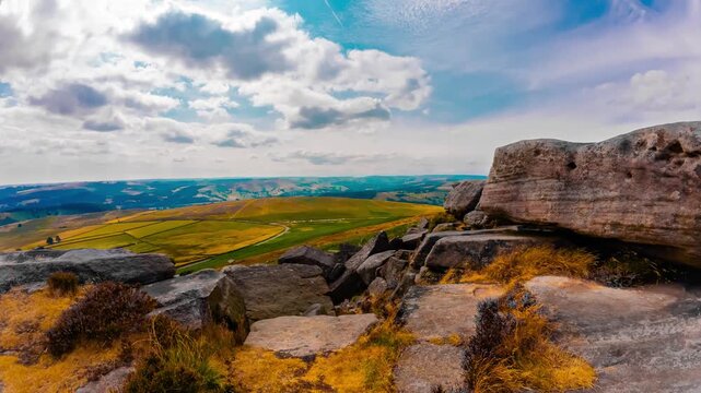 Timelapse Heather and gritstone rocks above agricultural valley beneath cumulus clouds. Moorland terrain with sandstone outcrops green fields and distant hills under summer sky time lapse. Heather