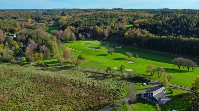 Aerial view of green golf course fairways and bunkers surrounded by forest in autumn