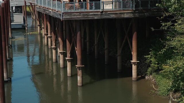 Restaurant on stilts above river with reflections shows waterfront architecture, support pillars above water and a calm urban riverside atmosphere during daytime