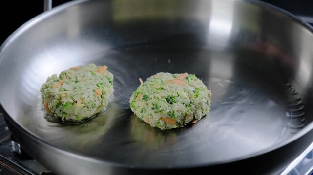 Hand cooking vegetable fritters with spatula in stainless steel pan on stove, bright kitchen, Cooking location.
