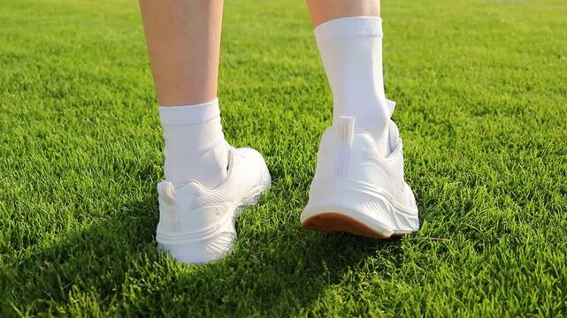 Female athlete takes off sneaker and sock to inspect a heel blister after sports training on a football stadium field. Close up of foot discomfort from intensive exercise, improper footwear, injury