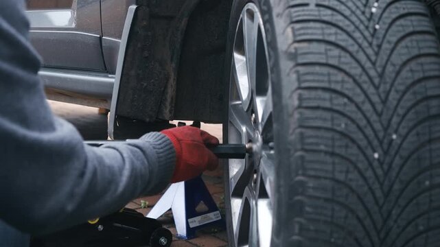 Gloved hands tightening wheel nuts with lug wrench during passenger car wheel installation. Automotive reassembly after brake repair with mechanic securing alloy rim fasteners on lifted vehicle. Tire