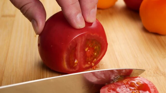 A chef uses a sharp knife to slice a ripe red tomato into juicy pieces on a wooden cutting board, with blurred whole tomatoes in the background under cinematic lighting.