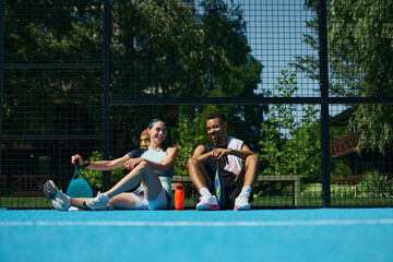 Naklejka premium Padel partners enjoying quiet rest on sunny court after recreational workout. Concept of outdoor wellbeing, active relaxation, healthy weekend routine.