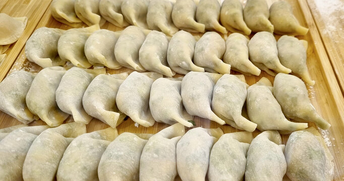 Rows of freshly handmade raw Chinese dumplings dusted with flour on a bamboo board. Authentic Asian cuisine preparation and traditional food background. Top view close up of jiaozi and potstickers.
