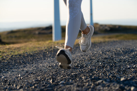A white woman running on a gravel trail near wind turbines in Galicia