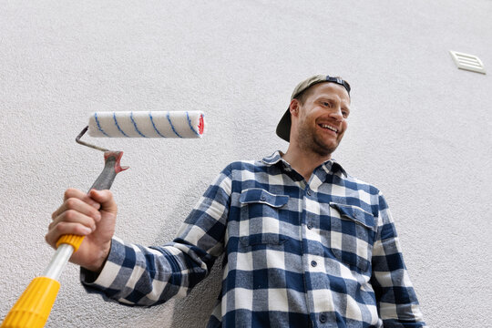 Smiling man holding paint roller ready for house painting and renovation