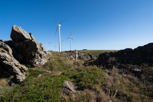 A white woman hiking near wind turbines in a rocky landscape