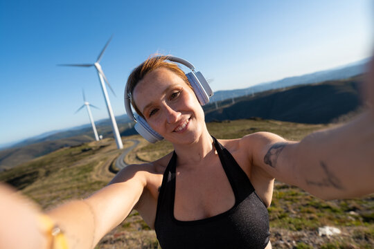 A white woman wearing headphones takes a selfie outdoors