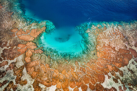Aerial view of orange and brown coral heads crowding a bright turquoise lagoon beside deep blue ocean water