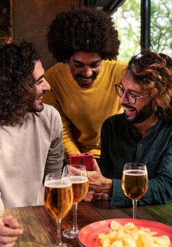 Multiethnic group of male friends together in a bar drinking beer and watching social media on one phone. Vertical image.