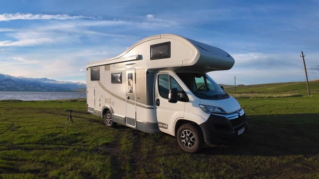 white recreational motorhome car parked on beautiful green field with picturesque Paravani Lake in Georgia mountains in background, demonstrating concept of nomadic lifestyle during scenic road trip