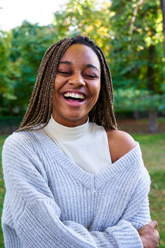 Vertical portrait of a cheerful young African American woman with big smile, standing outdoors in a public park.