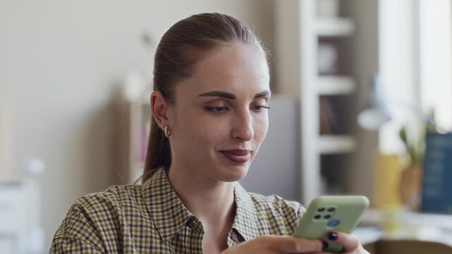 Caucasian young adult woman recording voice message on smartphone in modern office. Clip is ideal for corporate communication, mobile technology, and remote work marketing campaigns