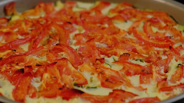 Close-up of a baked dish with tomato slices on creamy egg mixture in a baking dish, cooking indoors in a kitchen setting.