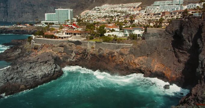 SPAIN CANARY ISLANDs TENERIFE 2023 April: Helicopter rescue operation. Rescuer lowered to the rocky shore over stormy ocean. Man hanging from the winch rope to retrieve a injured person.