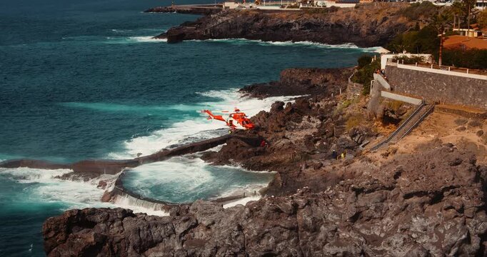 TENERIFE, CANARY ISLANDS, SPAIN, 2023 April: Medical helicopter landing on rocky volcanic shore for rescue operation. Aviation provides first aid to the injured. Stormy ocean beach.