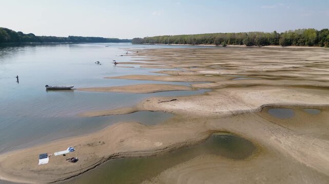 APATIN, SERBIA - AUGUST 4, 2026: Aerial drone video of people sunbathing and swimming on sandbars surrounded by low water level pools on the Danube River near Apatin during extreme summer heatwave.
