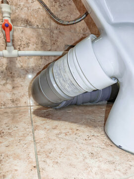 Toilet sewer connection with white corrugated plastic pipe and grey fitting. Plumbing system installation in domestic bathroom. Maintenance of drainage component for sanitary equipment