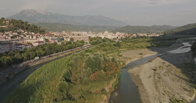 Berat Albania Aerial v1 low flyover along the Osum River, revealing lush riverbanks, downtown cityscape and mountain scenery at sunset - Shot with Mavic 3 Pro Cine - July 11th 2024