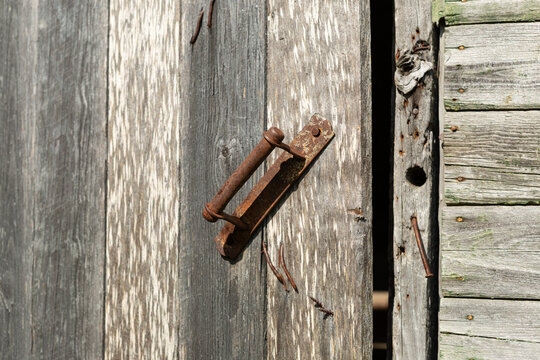 An old wooden front door to a country house with a rusty iron handle. The door is slightly ajar, and there is no lock.