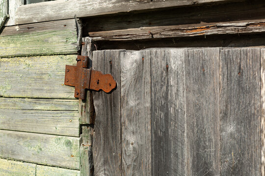 A rusty iron hinge on the old, wooden, slightly askew door of a village house.