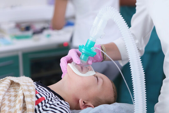 Small child under anesthesia. Anesthesiologist holds breathing mask on hild's face. Child feels nothing, does not move, and does not experience pain. Protecting child from stress and pain. Medical pro