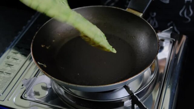 Hands cooking green vegetable fritters in a dark frying pan on a stainless steel stove, turning them with a spatula until golden brown, in a kitchen during daytime.