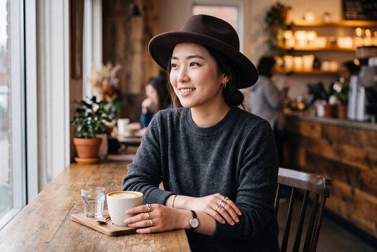 Young woman portrait in a cozy cafe with coffee and natural window light for lifestyle blog and social media background